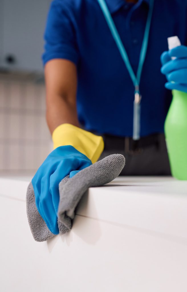 Gloved hand wiping a skirting board with a microfiber cloth