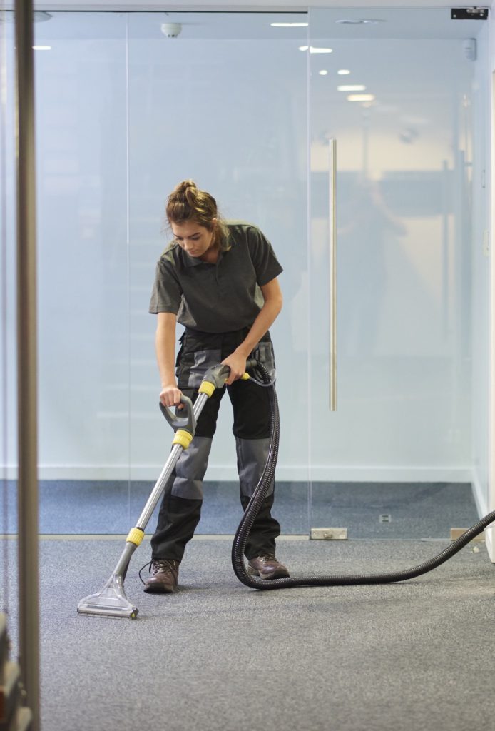 Cleaner using a floor machine beside a glass office partition