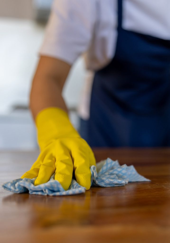 Gloved hands wiping a wooden table with a blue cloth
