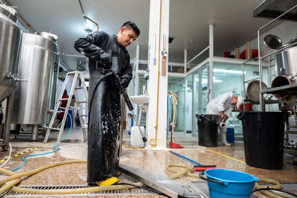 Worker in protective coveralls cleaning around industrial tanks