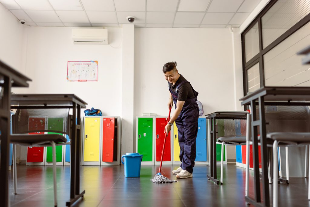 Cleaner mopping a classroom floor beside coloured lockers