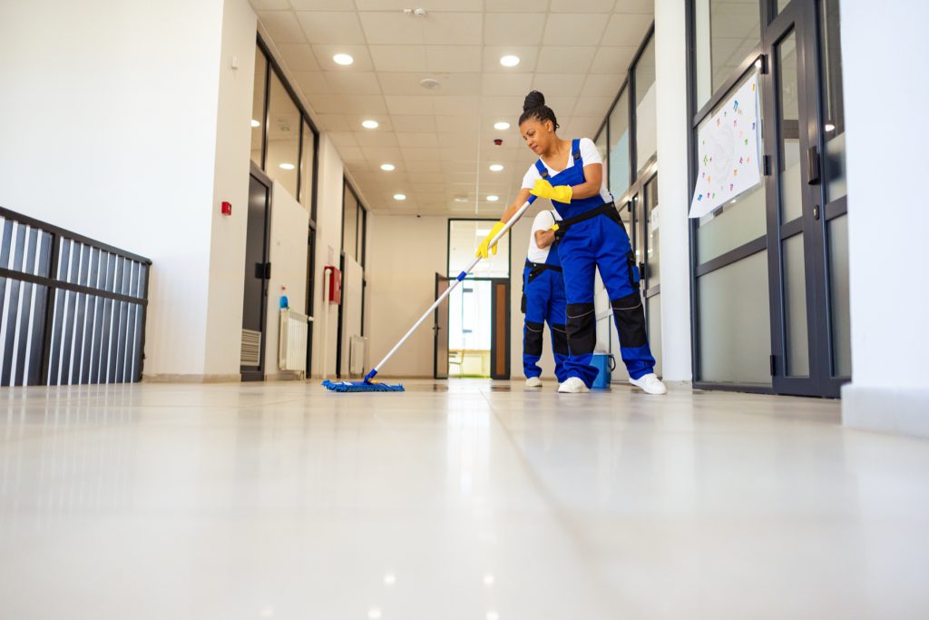 Two cleaners mopping a school corridor beside a wet floor sign