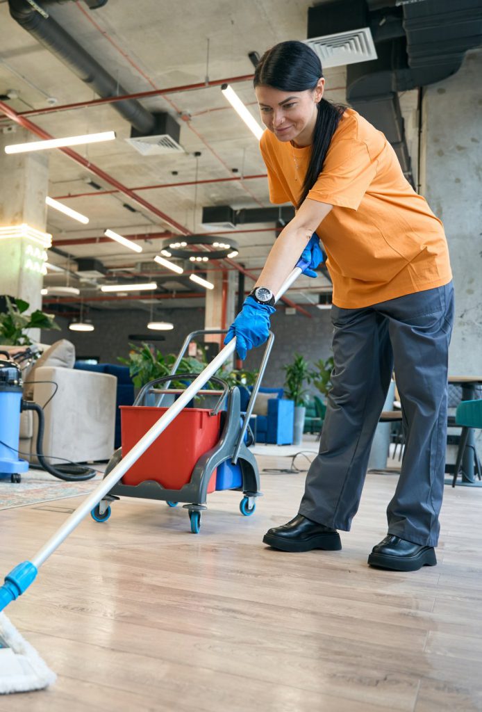 Cleaner in orange workwear flat-mopping a wooden office floor