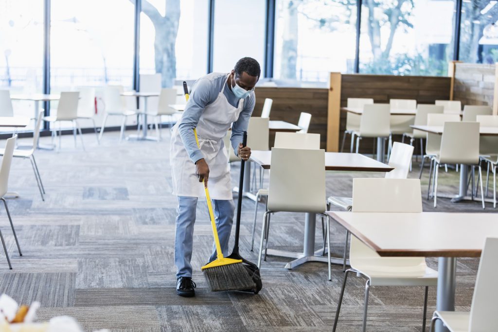 Cleaner sweeping a carpeted canteen floor between tables