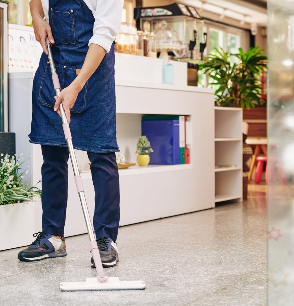 Cleaner flat-mopping a floor beside a reception counter