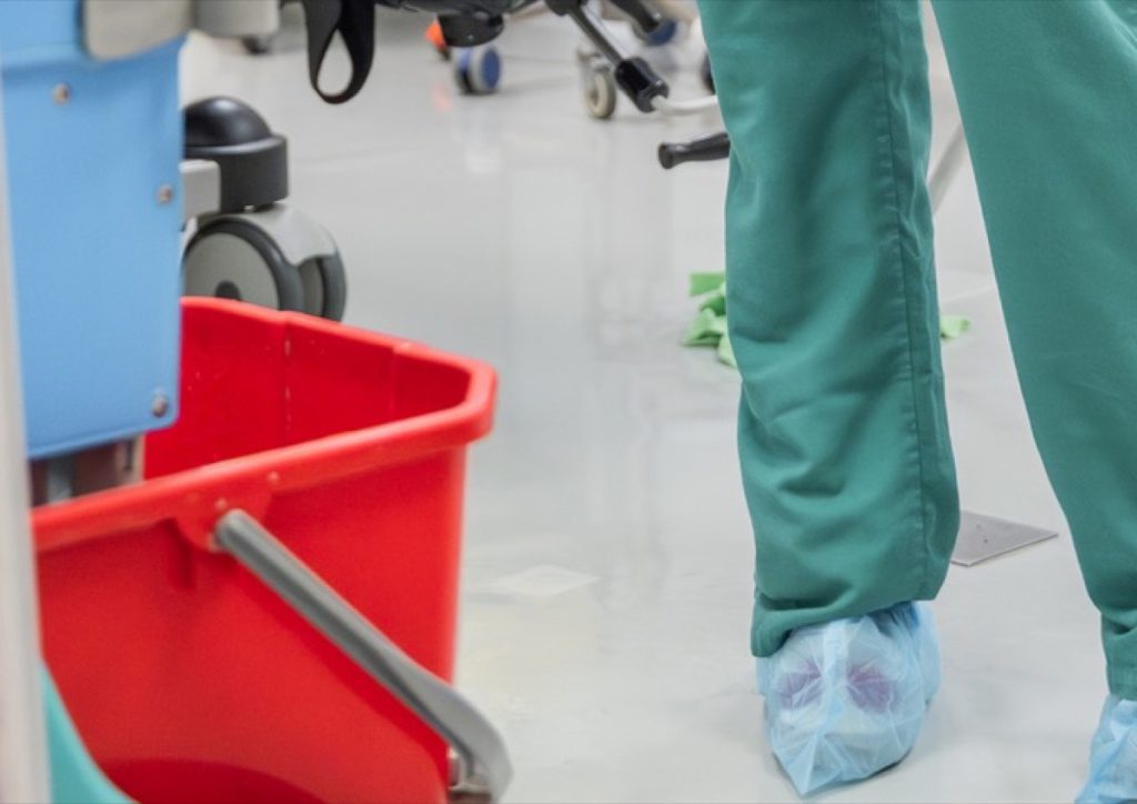 Red mop bucket beside a cleaner in scrubs and shoe covers