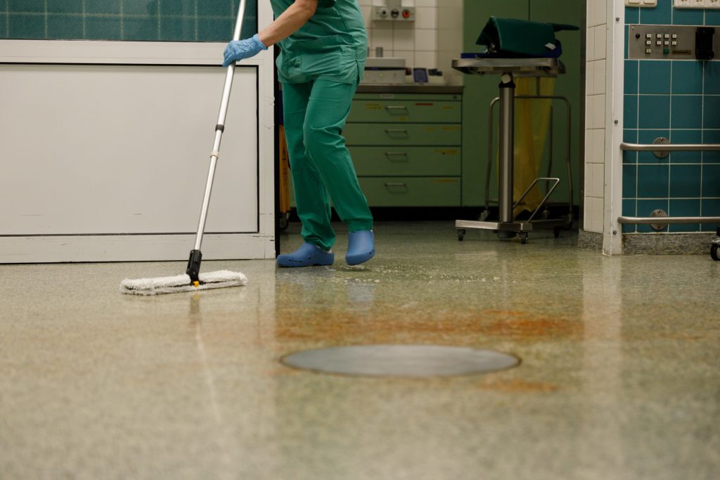 Cleaner in green scrubs flat-mopping a clinical floor