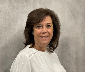 Studio headshot of Elizabeth Figueiredo, shoulder-length brown hair and a white blouse, against a grey backdrop