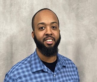 Studio headshot of Elton Monteiro, full beard and a blue checked shirt, against a grey backdrop