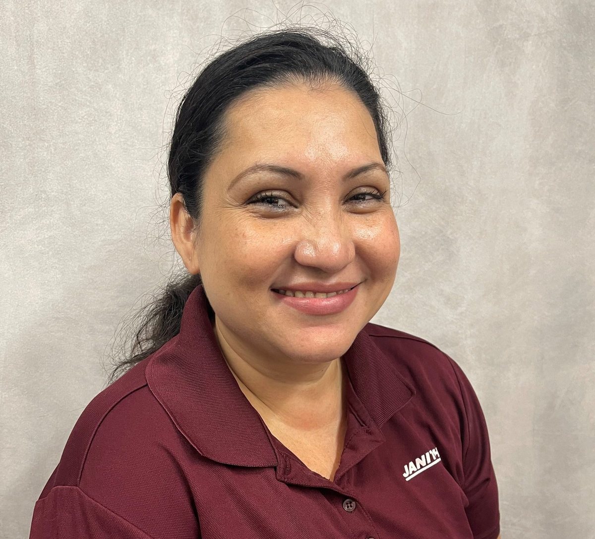 Studio headshot of Ingrid Rivera, dark hair tied back, in a maroon Janitech polo shirt