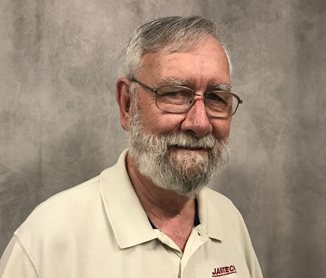 Studio headshot of Jim Heywood, white beard and glasses, in a cream Janitech polo shirt