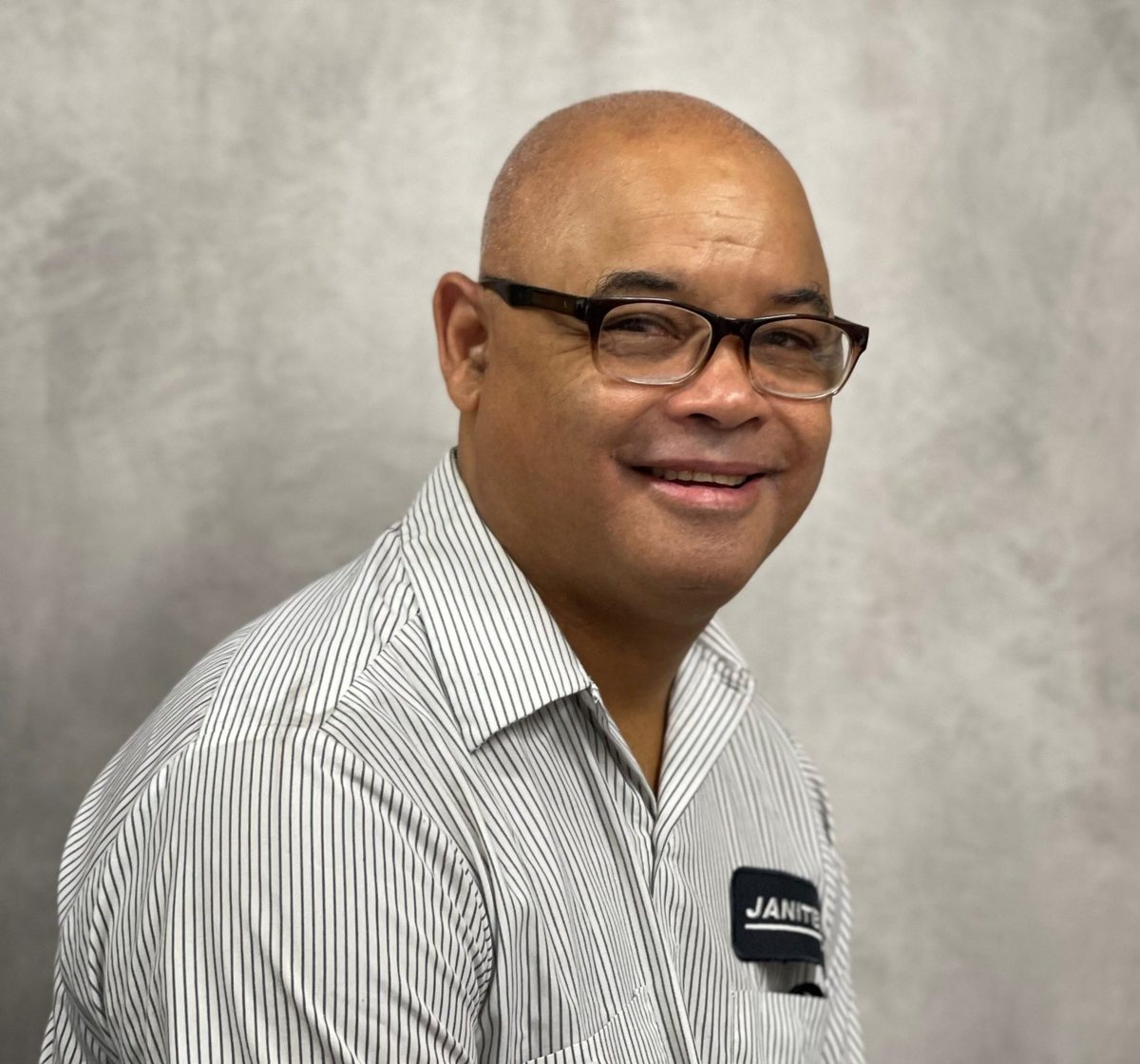 Studio headshot of Joselito Knapp, glasses and a striped shirt with a Janitech name badge